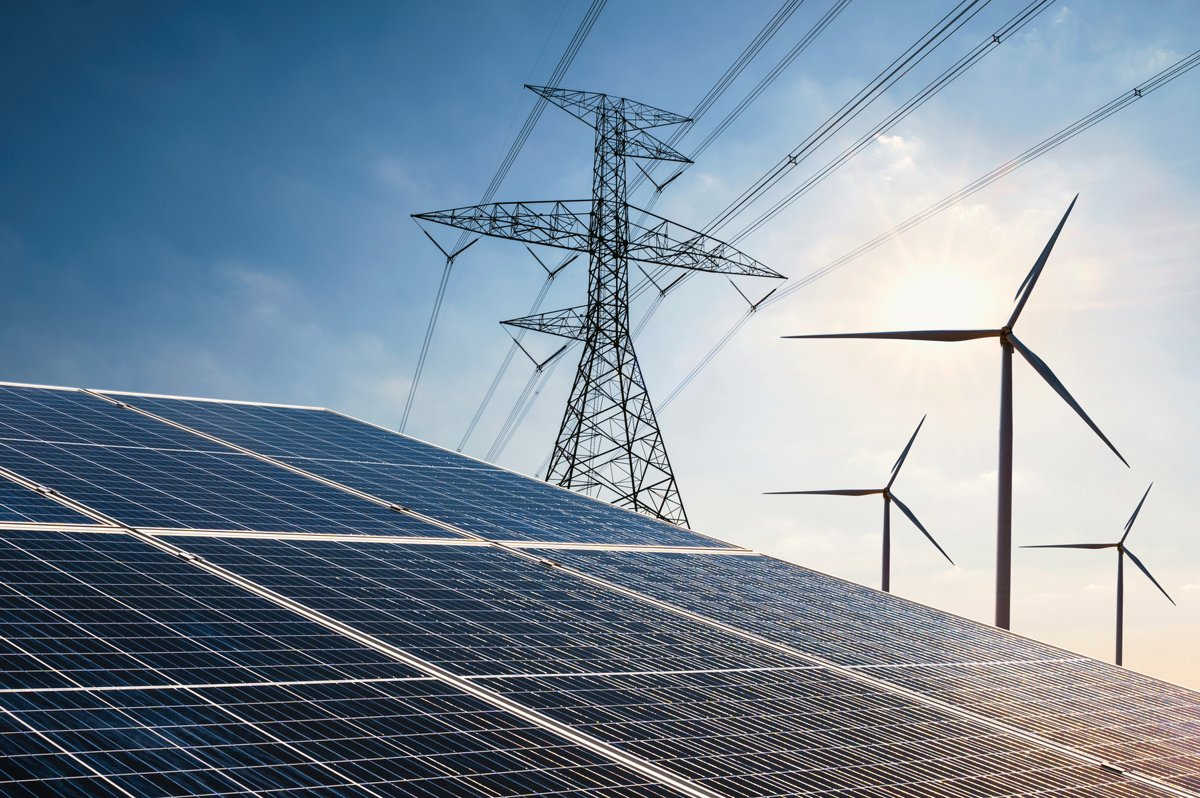 Solar panels, a transmission pylon and wind turbines against a bright sky